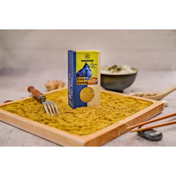 Easy Goreng Gewürz lose sowie in der Packung mit Sichtfenster und Illustration mit einem blauem Affen der aus einer Schlüssel Nudeln isst, auf hellgrünem Hintergrund und dem Schriftzug: "Für gebratenen Reis und Nudeln".