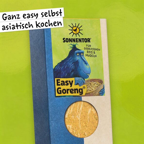 Easy Goreng Gewürz in der Packung mit Sichtfenster und Illustration mit dem Schriftzug: "Ganz easy selbst asiatisch kochen" und einem blauem Affen der aus einer Schlüssel Nudeln isst auf hellgrünem Hintergrund.